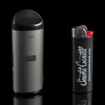 Black cannabis vaporizer pen and lighter with “Smoke Cartel” branding, displayed on a reflective surface.