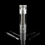 Silver cannabis vaporizer with glass chamber and cleaning tools on a reflective surface.