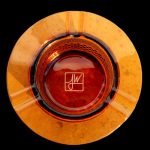 Overhead view of an orange glass ashtray with a signature etched in the center.