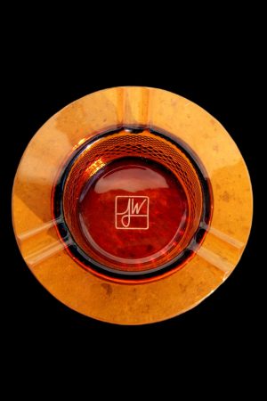 Overhead view of an orange glass ashtray with a signature etched in the center.