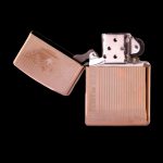 Open gold-toned lighter with engraved vertical lines on a black background.