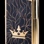 Gold Zippo lighter with a black background and a golden cannabis leaf within a crown design.