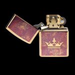 Gold lighter with a cannabis leaf-topped crown design, open to reveal the wick.