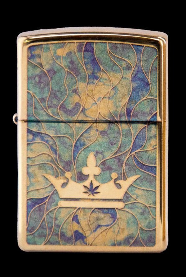 Gold Zippo lighter with a raised cannabis leaf within a golden crown design on a swirling teal and gold background.