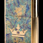 Gold Zippo lighter with a swirling teal and gold pattern and a crown featuring a cannabis leaf.