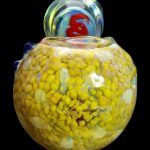Yellow and red speckled glass cannabis water pipe against a black background.
