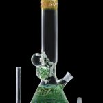 Green glass bong with intricate sculpted details, alongside a glass downstem and bowl.