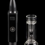 Black cannabis e-rig pen with a clear glass insert, studio shot on a reflective surface.