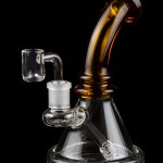 Amber and clear glass dab rig with quartz banger, isolated on a black background.