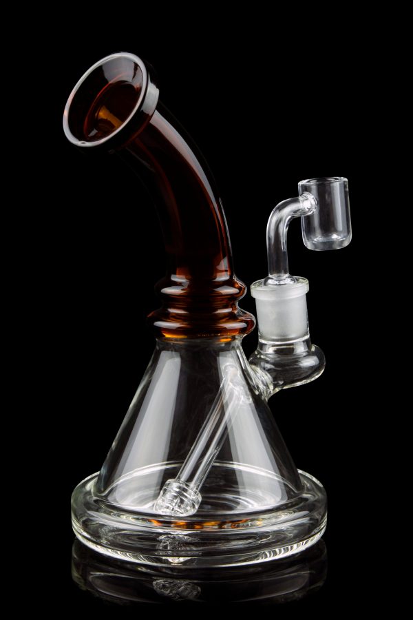A clear glass water pipe (rig) with a colored mouthpiece and a quartz nail for vaporizing concentrates, isolated on a black background.
