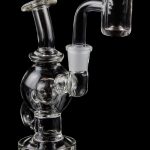 Clear glass dab rig with a quartz banger, isolated on a black background.