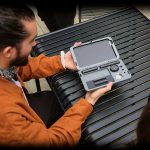 Man holding a grey cannabis accessory case open on a slatted surface, revealing organized compartments.