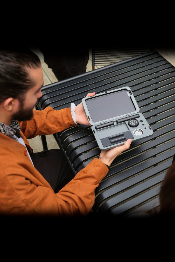 Man holding a grey cannabis accessory case open on a slatted surface, revealing organized compartments.