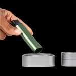 Green cannabis vape pen being inserted into a silver charging base, with a second base visible beside it.
