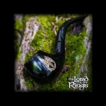 A green glass pipe with gold detailing rests against a mossy tree trunk, framed by a dark vignette and featuring ""The Lord of the Rings"" logo."