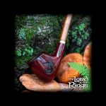 A carved wooden pipe rests in a hand against a blurred green forest backdrop, with "The Lord of the Rings" logo at the bottom.