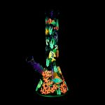 Glowing glass water pipe decorated with vibrant coral reef and fish designs against a black background.
