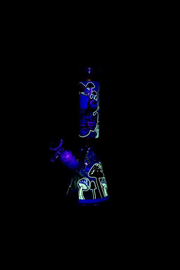 Glowing glass water pipe with psychedelic mushroom and face designs against a black background.