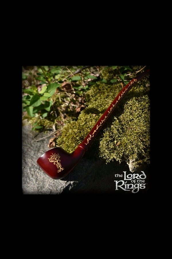 A long, intricately carved wooden pipe resembling a stylized branch lies on moss, with “The Lord of the Rings” logo visible below.