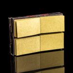 Gold rolling paper booklets stacked with a mirrored reflection on a black background.
