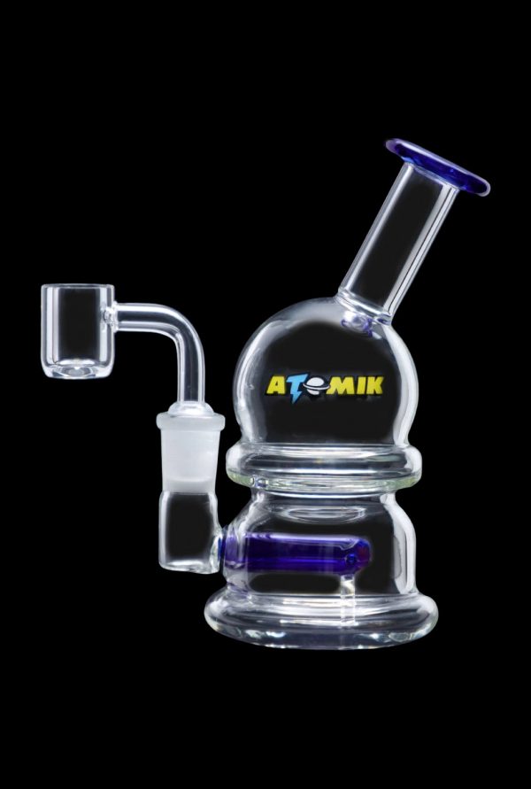 Clear glass dab rig with blue accents and a quartz nail, branded "ATOMIK".