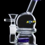 Clear glass bubbler with blue accents and "ATOMIC" lettering, used for smoking cannabis.