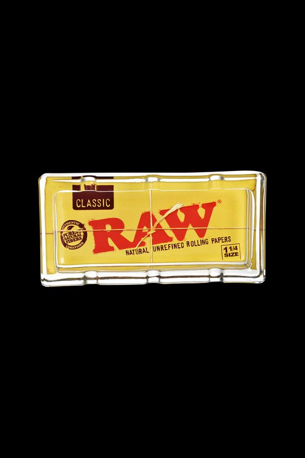 The RAW Classic Pack Glass Ashtray is shown in a close-up, angled view with visible branding on a black background.