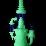 Glowing green glass water pipe (rig) with purple accents against a black background.