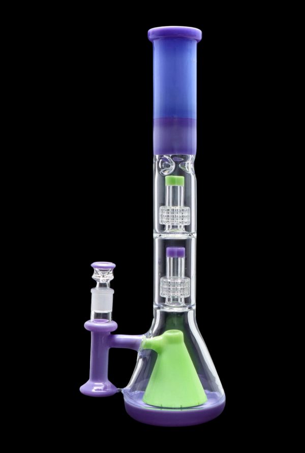 A vibrant, multi-chambered glass bong with a green base, purple midsection, and blue mouthpiece, accompanied by a separate glass pipe.