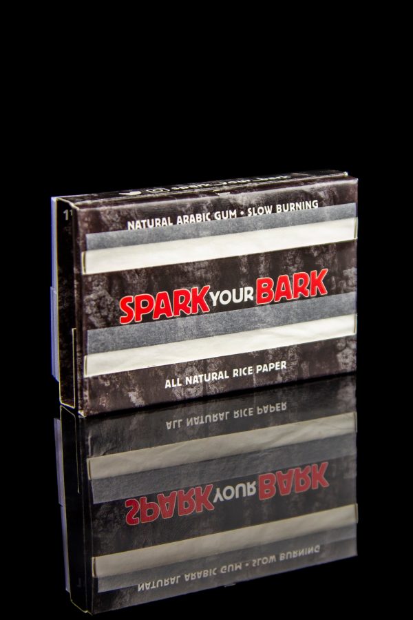 A pack of "Spark Your Bark" natural rice rolling papers with a woodgrain texture, set against a black background.