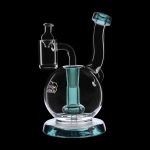 Clear glass dab rig with teal accents, featuring a bubbler base and accompanying glass carb cap.