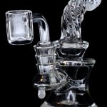 Clear glass dab rig with intricate swirls and a quartz banger, isolated on a black background.