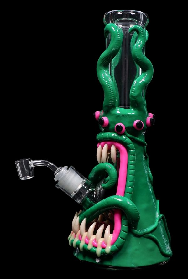 Green glass water pipe shaped like a monster with a pink tongue and exposed teeth, accompanied by a quartz banger.