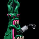 A vibrant green glass rig shaped like a monster with a wide-open mouth, pink tongue, and multiple tentacles, featuring a quartz banger for dabbing cannabis concentrates.