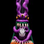 A vibrant glass water pipe shaped like a monster, featuring purple tentacles, glowing green eyes, and a menacing grin with orange teeth.