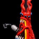 Red glass bong shaped like a cartoon monster with blue eyes, sharp teeth, and tentacle-like appendages, accompanied by a quartz nail.
