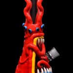 Red glass octopus-shaped water pipe with blue and white teeth, isolated on a black background.