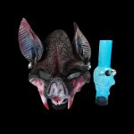 A spooky bat mask and blue glass pipe against a black background.