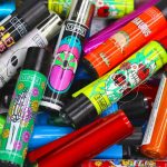 A colorful assortment of Clipper lighters with vibrant, psychedelic designs, scattered on a patterned surface.
