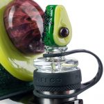 Close-up view of the Empire Glassworks Avocadope Carb Cap for Puffco Peak, showcasing its green, sculpted design against a blurred background.