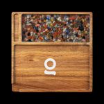 Wooden cannabis accessory box filled with colorful crystal-like pieces, featuring a circular logo on the front.