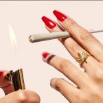 Close-up of manicured nails lighting a joint with a gold lighter.