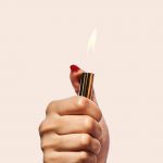 Hand holding a lit gold lighter, flame visible.