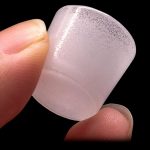 Close-up of a translucent, pink cannabis concentrate dab tool held between fingertips.