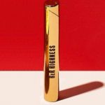 Gold cannabis vape pen with “Her Highness” text, casting a long shadow on a white surface against a red backdrop.