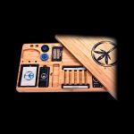 Wooden cannabis rolling tray with peace sign accents and compartments for accessories, displayed against a black background.