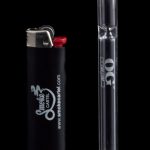 Glass pipe and lighter with branding for Smoke Cartel, reflecting on a black surface.