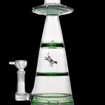A glass water pipe shaped like a UFO with a cowboy graphic inside, accompanied by a glass bowl.