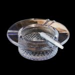 A clear glass ashtray with a partially smoked joint resting inside, set against a black background.