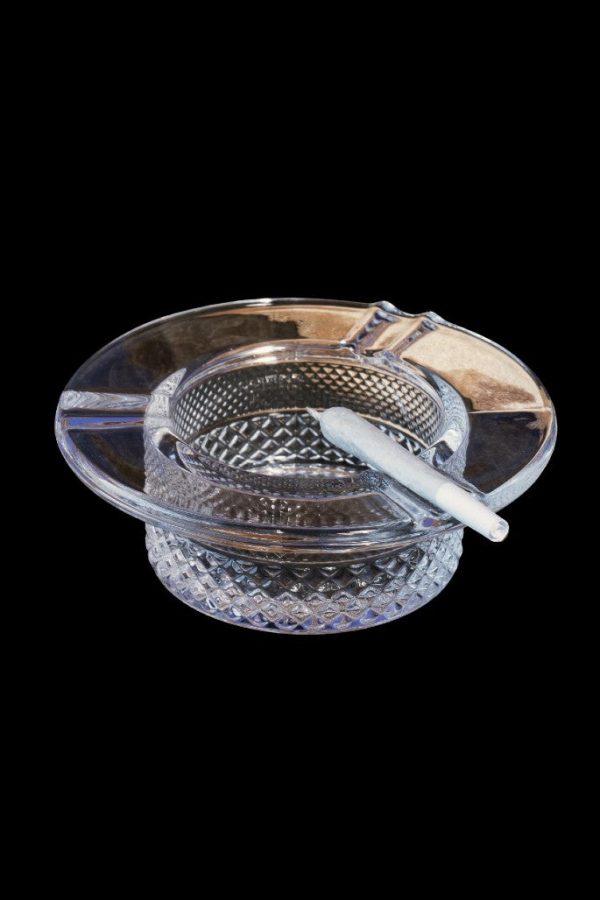 A clear glass ashtray with a partially smoked joint resting inside, set against a black background.
